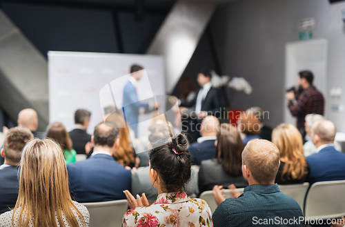 Image of Business team leader receiving award prize at best business project competition event. Business and entrepreneurship award ceremony theme. Focus on unrecognizable people in audience.