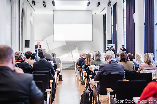 Image of Speaker giving a talk in conference hall at business event. Rear view of unrecognizable people in audience at the conference hall. Business and entrepreneurship concept.