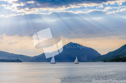 Image of sailboats in sailboats rays of light on the fjord with mountains