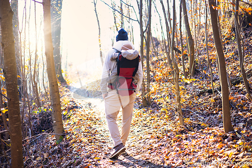 Image of Sporty father carrying his infant son wearing winter jumpsuit and cap in backpack carrier hiking in autumn forest.