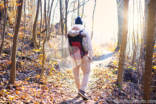 Image of Sporty father carrying his infant son wearing winter jumpsuit and cap in backpack carrier hiking in autumn forest.