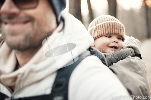 Image of Sporty father carrying his infant son wearing winter jumpsuit and cap in backpack carrier hiking in autumn forest.