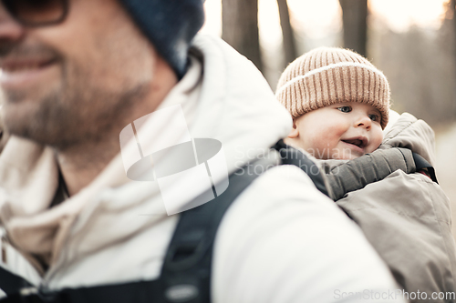 Image of Sporty father carrying his infant son wearing winter jumpsuit and cap in backpack carrier hiking in autumn forest.