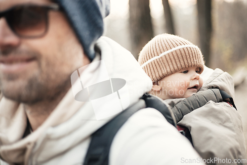 Image of Sporty father carrying his infant son wearing winter jumpsuit and cap in backpack carrier hiking in autumn forest.