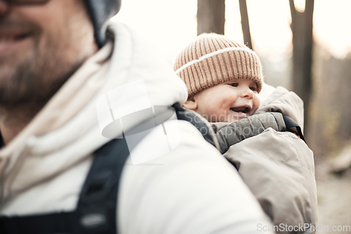 Image of Sporty father carrying his infant son wearing winter jumpsuit and cap in backpack carrier hiking in autumn forest.