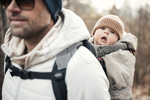 Image of Sporty father carrying his infant son wearing winter jumpsuit and cap in backpack carrier hiking in autumn forest.