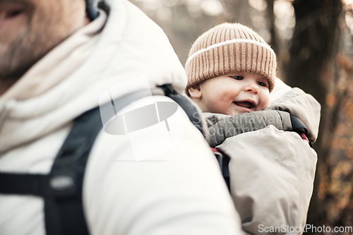 Image of Sporty father carrying his infant son wearing winter jumpsuit and cap in backpack carrier hiking in autumn forest.