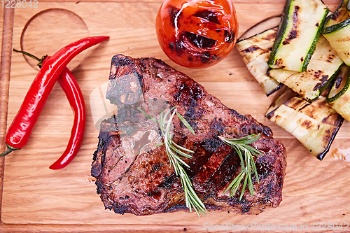 Image of Grilled T-Bone Steak on serving board on wooden background