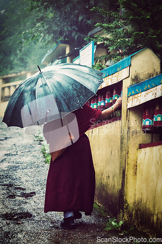 Image of Buddhist monk with umbrella spinning prayer wheels