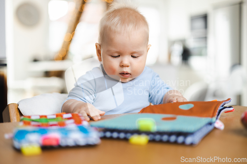 Image of Happy infant sitting at dining table and playing with his toy in traditional scandinavian designer wooden high chair in modern bright atic home. Cute baby playing with toys