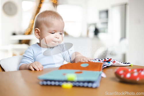 Image of Happy infant sitting at dining table and playing with his toy in traditional scandinavian designer wooden high chair in modern bright atic home. Cute baby playing with toys