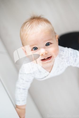 Image of top down view of cheerful baby boy infant taking first steps holding to kitchen drawer at home. Cute baby boy learning to walk