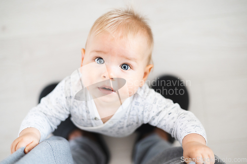 Image of Top down view of cheerful baby boy infant taking first steps holding to father's sweatpants at home. Cute baby boy learning to walk