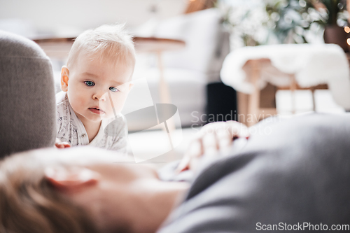 Image of Happy family moments. Mother lying comfortably on children's mat playing with her baby boy watching and suppervising his first steps. Positive human emotions, feelings, joy.