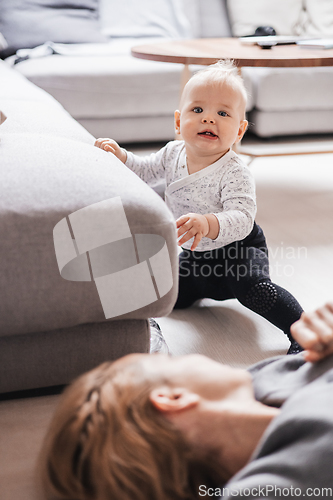 Image of Happy family moments. Mother lying comfortably on children's mat playing with her baby boy watching and suppervising his first steps. Positive human emotions, feelings, joy.