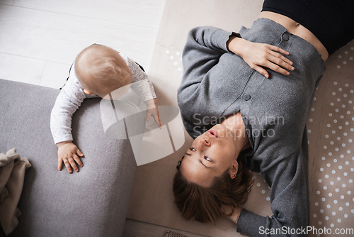 Image of Happy family moments. Mother lying comfortably on children's mat playing with her baby boy watching and suppervising his first steps. Positive human emotions, feelings, joy.