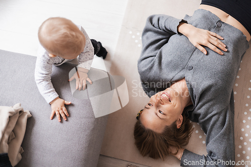 Image of Happy family moments. Mother lying comfortably on children's mat playing with her baby boy watching and suppervising his first steps. Positive human emotions, feelings, joy.