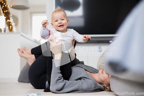 Image of Happy family moments. Mother lying comfortably on children's mat playing with her baby boy watching and suppervising his first steps. Positive human emotions, feelings, joy.