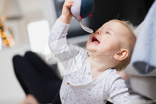 Image of Cute infant baby boy playing, crawling and standing up by living room sofa at home. Baby playing at home