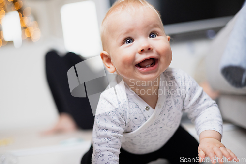 Image of Cute infant baby boy playing, crawling and standing up by living room sofa at home. Baby playing at home.