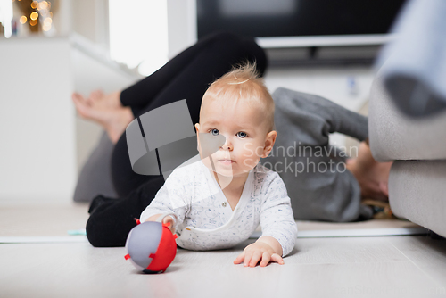 Image of Happy family moments. Mother lying comfortably on children's mat watching and suppervising her baby boy playinghis in living room. Positive human emotions, feelings, joy