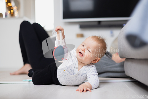 Image of Happy family moments. Mother lying comfortably on children's mat watching and suppervising her baby boy playinghis in living room. Positive human emotions, feelings, joy