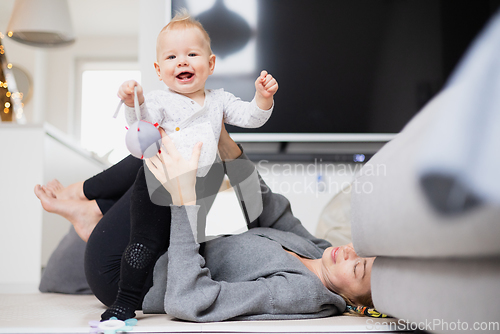 Image of Happy family moments. Mother lying comfortably on children's mat playing with her baby boy watching and suppervising his first steps. Positive human emotions, feelings, joy.