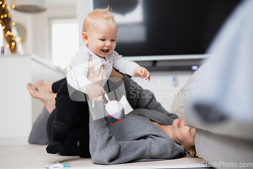 Image of Happy family moments. Mother lying comfortably on children's mat playing with her baby boy watching and suppervising his first steps. Positive human emotions, feelings, joy.