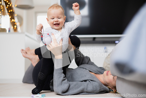 Image of Happy family moments. Mother lying comfortably on children's mat playing with her baby boy watching and suppervising his first steps. Positive human emotions, feelings, joy.