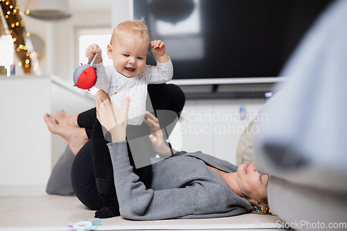 Image of Happy family moments. Mother lying comfortably on children's mat playing with her baby boy watching and suppervising his first steps. Positive human emotions, feelings, joy.