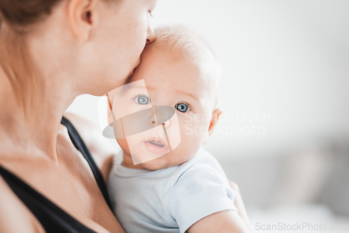 Image of Portrait of sweet baby resting in mothers arms, looking at camera. New mom holding and kissing little kid, embracing child with tenderness, love, care. Motherhood concept