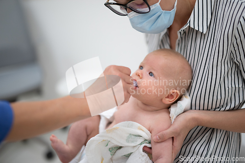 Image of Pediatrician administring oral vaccination against rotavirus infection to little baby in presence of his mother. Children health care and disease prevention