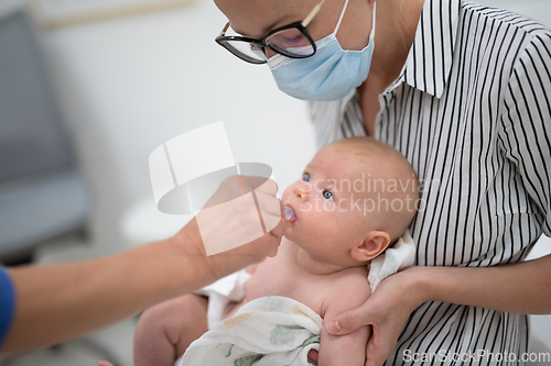 Image of Pediatrician administring oral vaccination against rotavirus infection to little baby in presence of his mother. Children health care and disease prevention