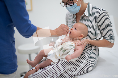 Image of Pediatrician administring oral vaccination against rotavirus infection to little baby in presence of his mother. Children health care and disease prevention