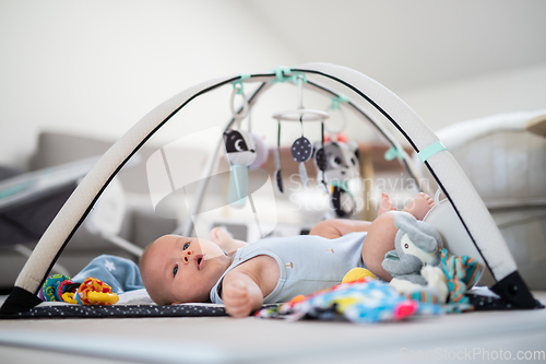 Image of Cute baby boy playing with hanging toys arch on mat at home Baby activity and play center for early infant development. Baby playing at home