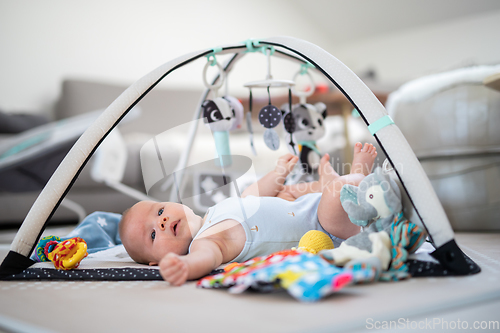 Image of Cute baby boy playing with hanging toys arch on mat at home Baby activity and play center for early infant development. Baby playing at home