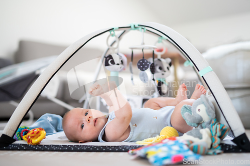 Image of Cute baby boy playing with hanging toys arch on mat at home Baby activity and play center for early infant development. Baby playing at home