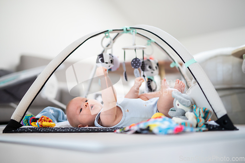 Image of Cute baby boy playing with hanging toys arch on mat at home Baby activity and play center for early infant development. Baby playing at home