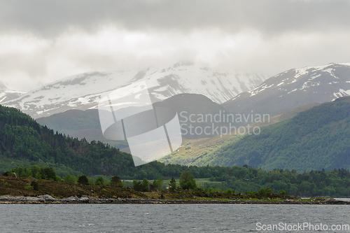 Image of snow-capped mountains with green trees and rays of sunshine brea