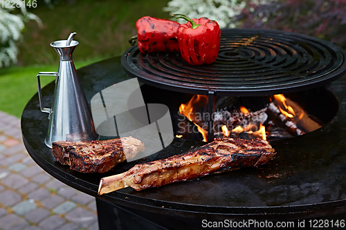 Image of Tomahawk rib beef steak and T-bone on hot black grill.