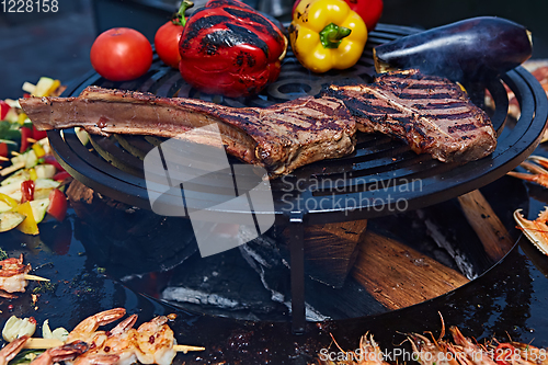 Image of Tomahawk rib beef steak and T-bone on hot black grill.