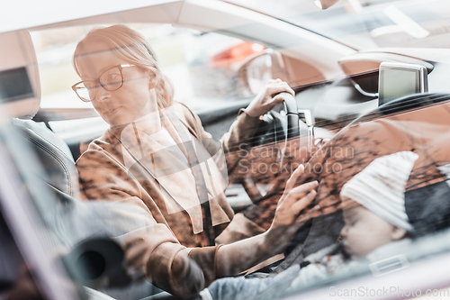 Image of Mother reversing family car, looking for free parking space while running errands with her baby sleeping in infant car seat by her site.