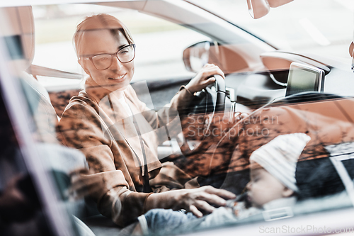 Image of Mother driving family car, running errands, while her baby sleeps in infant car seat by her site.