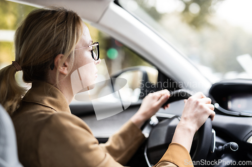 Image of Business woman driving a car to work. Female driver steering car on the road