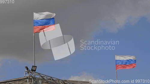 Image of Russian flag on the flagpole waving in the wind against a blue sky with clouds