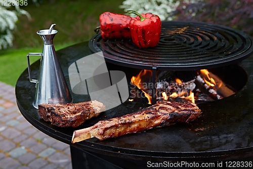 Image of Tomahawk rib beef steak and T-bone on hot black grill.