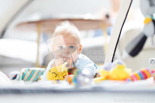 Image of Cute baby boy playing with hanging toys arch on mat at home Baby activity and play center for early infant development. Baby playing at home