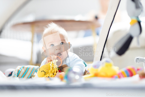 Image of Cute baby boy playing with hanging toys arch on mat at home Baby activity and play center for early infant development. Baby playing at home