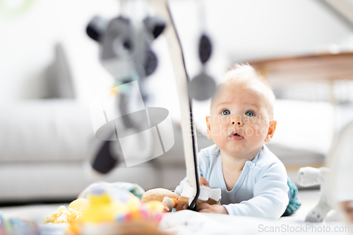 Image of Cute baby boy playing with hanging toys arch on mat at home Baby activity and play center for early infant development. Baby playing at home