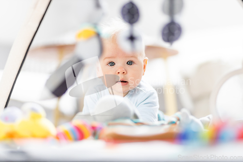 Image of Cute baby boy playing with hanging toys arch on mat at home Baby activity and play center for early infant development. Baby playing at home